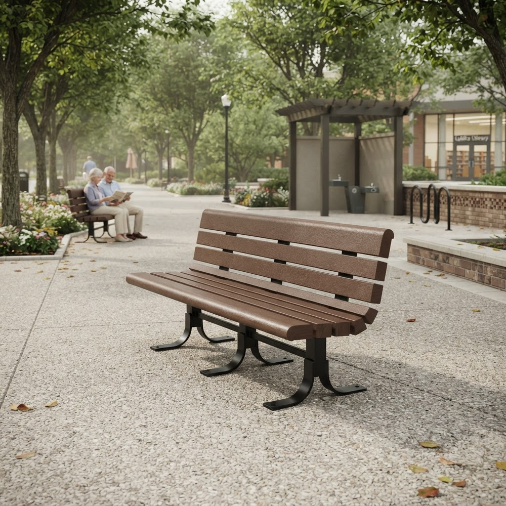 A brown slatted outdoor bench with black metal legs sits on a paved walkway in a park-like setting with trees, a small shelter, and a couple seated in the background.