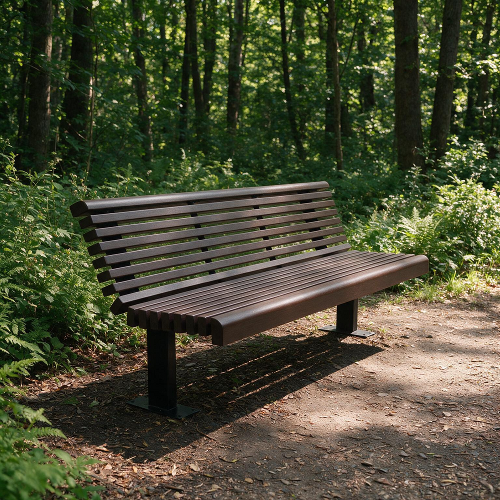 A dark brown slatted outdoor park bench placed on a dirt path surrounded by a dense green forest.