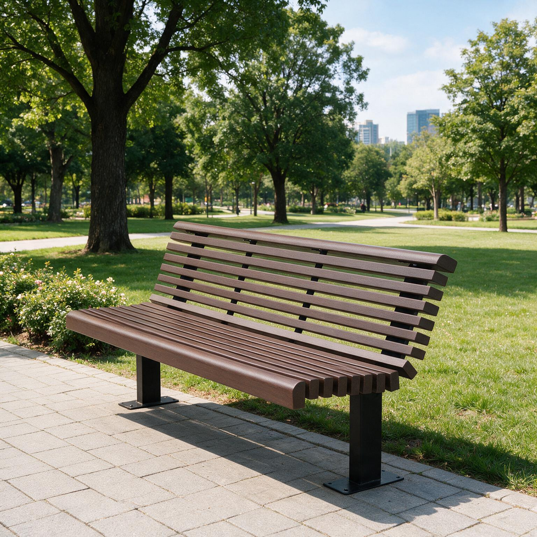 A modern slatted park bench in brown and black sits on a paved path in a sunny park with green grass, trees, and distant buildings.