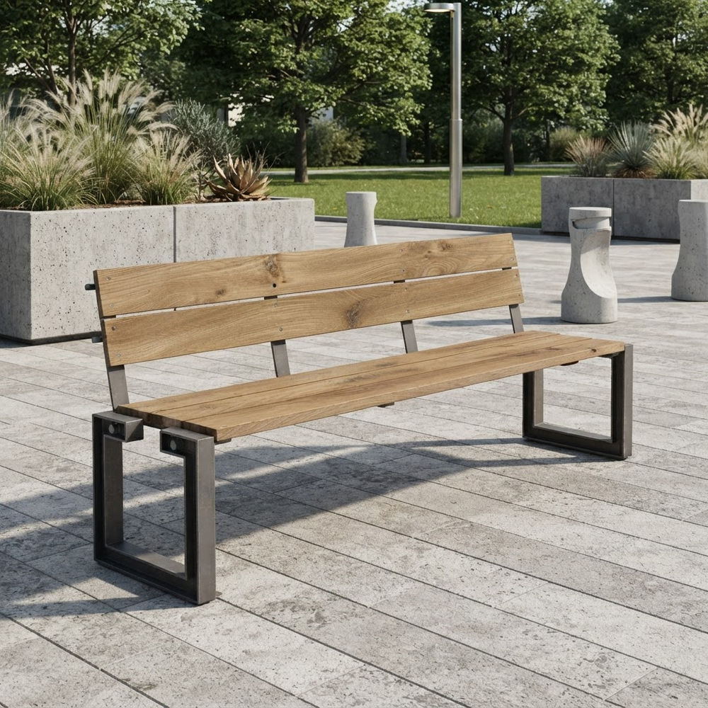 A modern outdoor park bench with light brown wooden slats and a dark gray metal frame, situated on a paved plaza with trees and planters in the background.