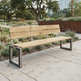 Outdoor park bench with a light natural wood seat and back slats and a dark metal frame, placed on a concrete walkway in a landscaped garden area.