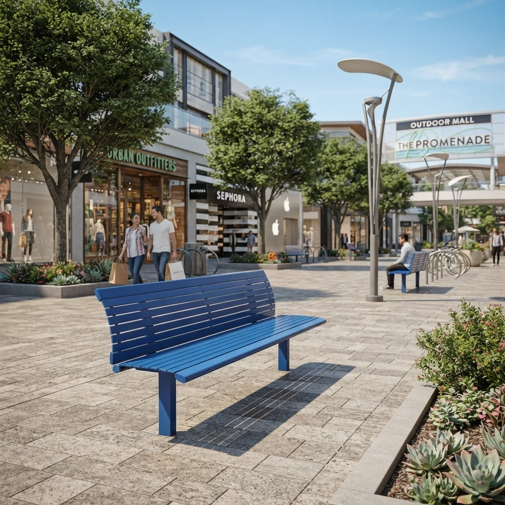 A bright blue outdoor bench in a modern paved shopping plaza with storefronts, trees, pedestrians, and streetlights. The scene appears to be a real environment rather than a clean studio product shot, so this fits Lifestyle rather than Product/Packaging.