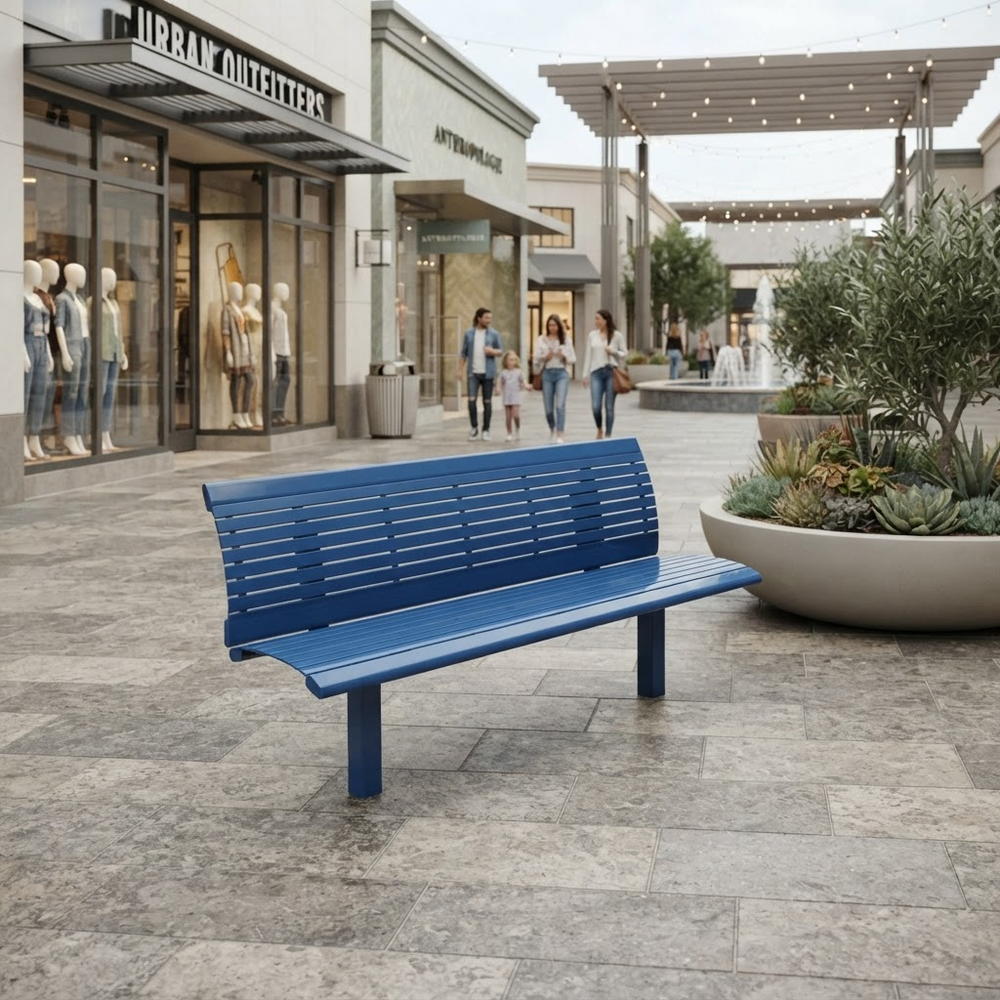 A blue slatted outdoor bench placed on a paved shopping plaza walkway, with storefronts, pedestrians, and planters visible in the background.