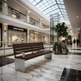 A modern wooden bench with a brushed silver metal base sits in a luxury shopping mall atrium with marble floors, potted plants, and visible Louis Vuitton and Gucci storefronts in the background.