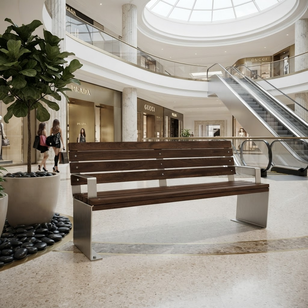 A modern wooden and metal outdoor-style bench placed in a spacious, sunlit shopping mall atrium with escalators, storefronts, and potted plants visible in the background.