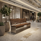 A modern wooden park bench with a brushed stainless steel base is situated in a spacious, upscale shopping mall plaza. Large potted green plants and storefronts like Aurora Fine Jewelry and Bottega Veneta are visible in the background, with a few shoppers walking in the distance.