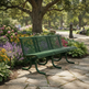 A green metal park bench with curved legs sits on a stone pathway in a lush garden park, surrounded by colorful flowers, green foliage, and trees in the background.