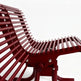 A close-up studio shot of a modern lounge chair with a curved back and seat made of parallel reddish-brown slats, set against a plain white background.