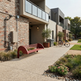 A modern outdoor residential courtyard with a curved red bench in the foreground, a concrete walkway, landscaped planters, and contemporary brick and concrete apartment buildings in the background.