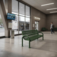 A green metal bench sits in a modern bus station interior with large windows, a bus outside, a map on a pole, and a person walking in the background.