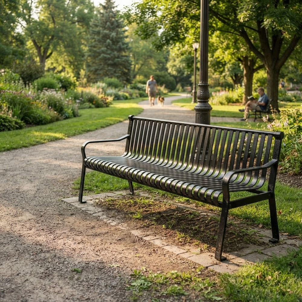 A dark metal park bench with a slatted back and seat, positioned on a paved path in a lush green park with trees, grass, and distant people.
