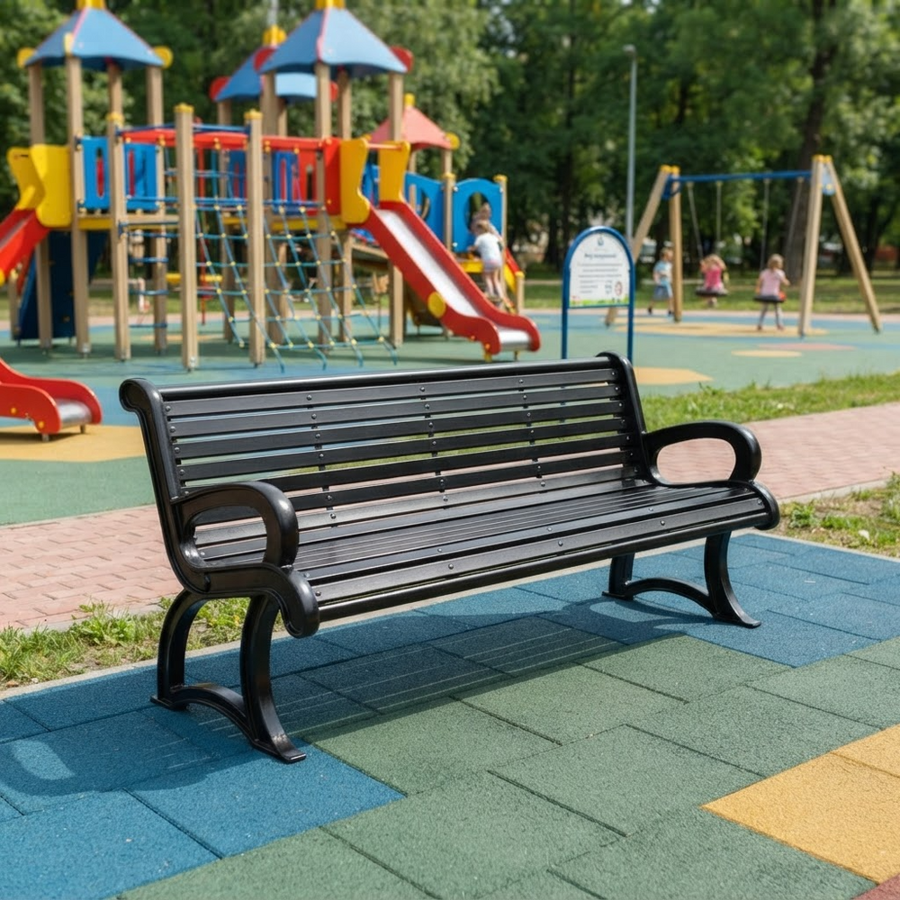 A black slatted park bench with curved armrests sits on colorful blue, green, and yellow rubberized playground flooring in front of a children's playset with trees in the background.