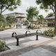 A modern black metal park bench with curved armrests situated on a paved walkway in a landscaped public park. Trees, planters, a playground, and a building are visible in the background, with a few people walking and sitting nearby.