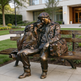 Bronze statue of two people sitting on a bench in front of a building.