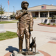 Bronze statue of a soldier with a dog in front of a building with an American flag.