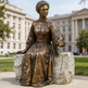 Detailed bronze artwork depicting a seated female figure with outstretched hand