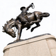 Bronze artwork of a cowboy gripping reins while riding a powerful bucking horse.