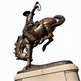 Detailed bronze rodeo sculpture showing a cowboy mid‑ride with lasso lifted high.