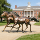 Bronze statues of two horses running in front of a brick building with columns.