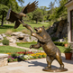 Bronze statue of a bear and an eagle in a garden setting with flowers and rocks.