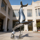 Sleek metallic sculpture featuring a whale in motion above a stylized human form