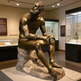 Bronze statue of a seated figure in a museum setting with informational displays.