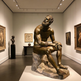 Bronze statue in a museum setting with paintings and sculptures on the walls.