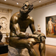 Bronze statue of a bearded man in a museum setting with other sculptures and art in the background.