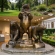Bronze statue of three bears on a pedestal with a garden and building in the background.
