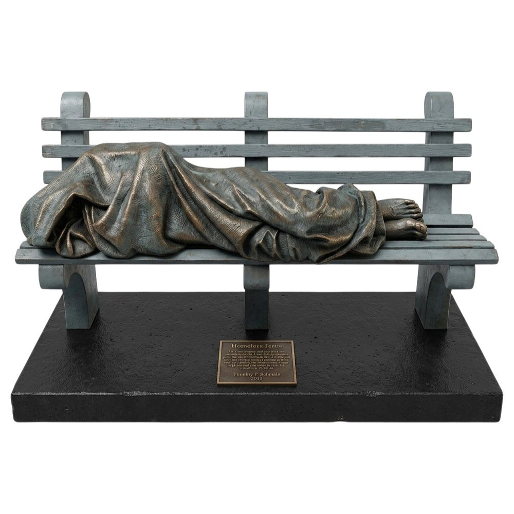 Statue of a person lying on a bench with a blanket, on a white background
Bronze Homeless Jesus sculpture lying on a bench with draped blanket