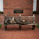 Bronze statue of a person on a bench with a quote plaque in the 
background.
Bronze Homeless Jesus sculpture lying on a bench with draped blanket