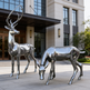 Two metallic deer sculptures in front of a building
Chrome animal sculptures depicting a standing deer and a grazing companion.
