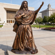 Bronze statue of a religious figure in front of a building with a clear sky