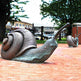 Bronze snail sculpture on a stone surface with trees and buildings in the background
Bronze artwork of a snail with extended antennae and sculpted ridges