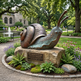 Bronze snail sculpture on a stone base in a park setting with people and buildings in the background.
Detailed metal snail statue featuring coiled shell and patterned body
