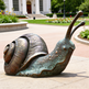 Bronze snail sculpture in an outdoor setting with a building and garden in the background
Sculpted bronze snail with intricate shell ridges and textured surface