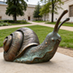 Bronze snail sculpture in front of a building with greenery
Decorative metal snail artwork featuring detailed craftsmanship
