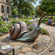 Large bronze snail sculpture in a park with people and a building in the background
Realistic bronze snail sculpture with patterned body and polished shell