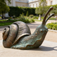 Bronze snail sculpture in a garden setting with a building in the background