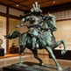 Bronze statue of a samurai on horseback in a museum setting
Metal samurai and horse sculpture with intricate armor detailing.”

