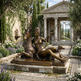 Bronze statue of a woman with a deer in a garden setting with classical architecture.