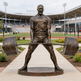 Bronze statue of a weightlifter in front of a stadium
Bronze fitness sculpture showing a man raising a loaded barbell