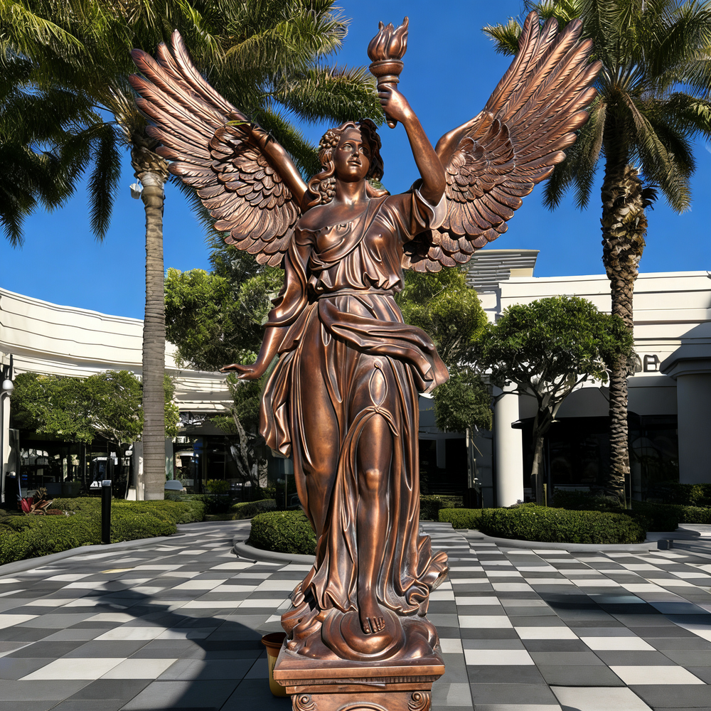 Bronze statue of an angel holding a torch in a plaza with palm trees and checkered floor.
Winged female figure in bronze with detailed drapery.
