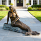 Bronze mermaid statue on a stone pedestal in front of a house.