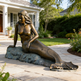 Bronze mermaid statue on a stone patio in front of a house