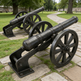 Two black cannons on wheels in a park setting with green grass and 
trees.
Cannon statue with cylindrical barrel and carriage wheels