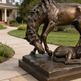 Bronze sculpture of a horse and a dog on a stone pedestal in a garden setting.