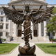 Bronze statue of an angel with wings spread in front of a classical building
Winged female figure with spread wings and symbolic ascension design