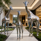 Three metallic giraffe sculptures in a modern indoor setting with a building and interior decor in the background.
Metallic giraffe trio with reflective surfaces and detailed patterns.