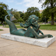 Bronze statue of a mermaid on a marble base in a park setting